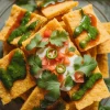 Perfect for gatherings or light meals, Dhokla Nachos are a deliciously healthy alternative to traditional nacho plates. Discover how to create this mouthwatering dish that brings together comfort and innovation in every bite.